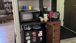 Una kitchenette funcional con microondas, cafetera y cajones para guardar objetos.