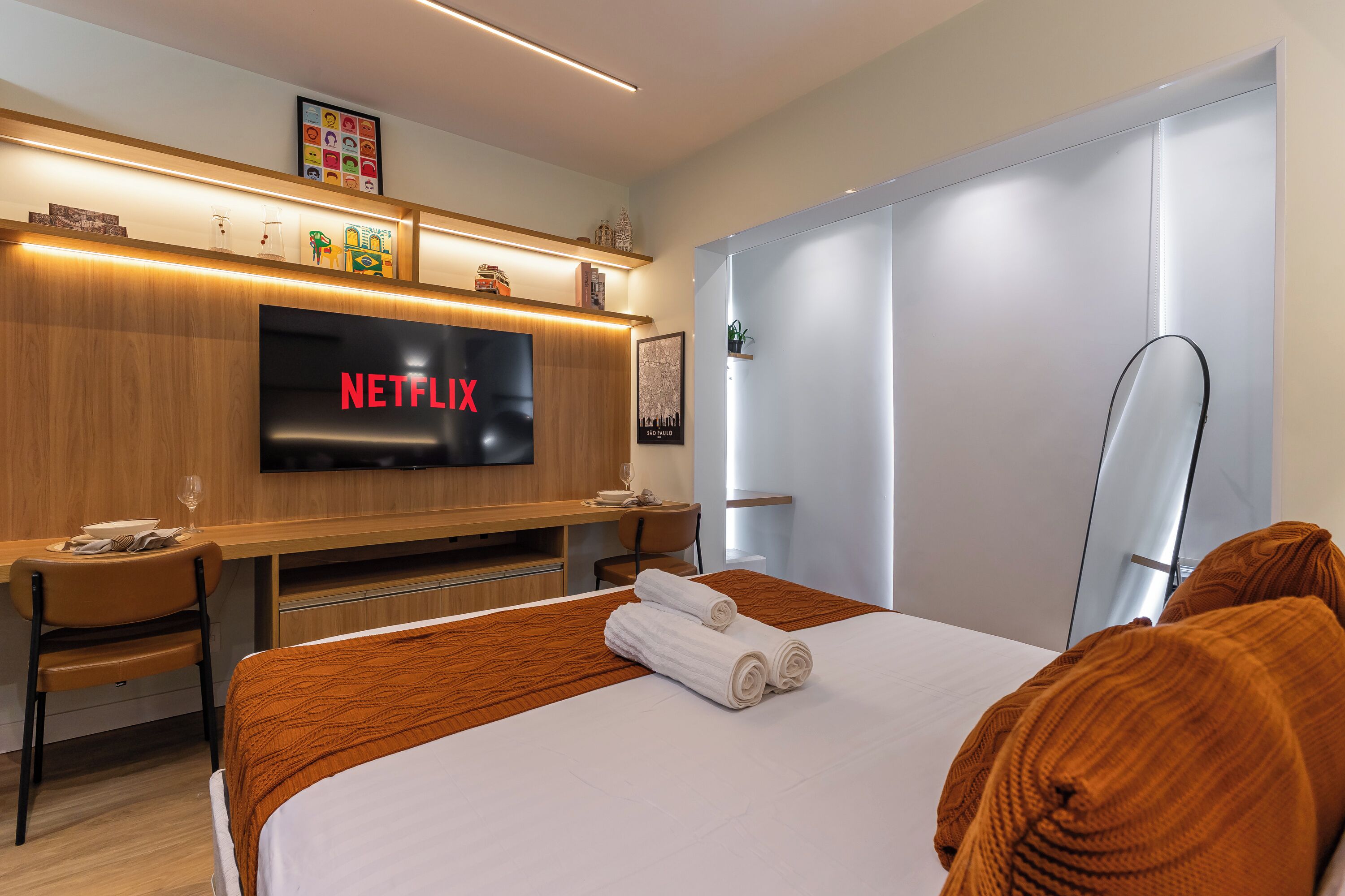 Una habitación de hotel moderna con una cama grande, un escritorio con un televisor de pantalla plana que muestra 'NETFLIX', una mesita con una copa de vino y una silla.