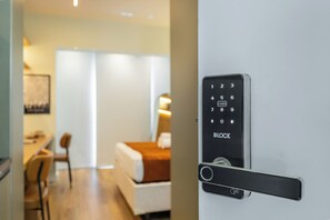 Een moderne hotelkamer met een digitaal slot op de deur, een bed, een bureau en een stoel.
