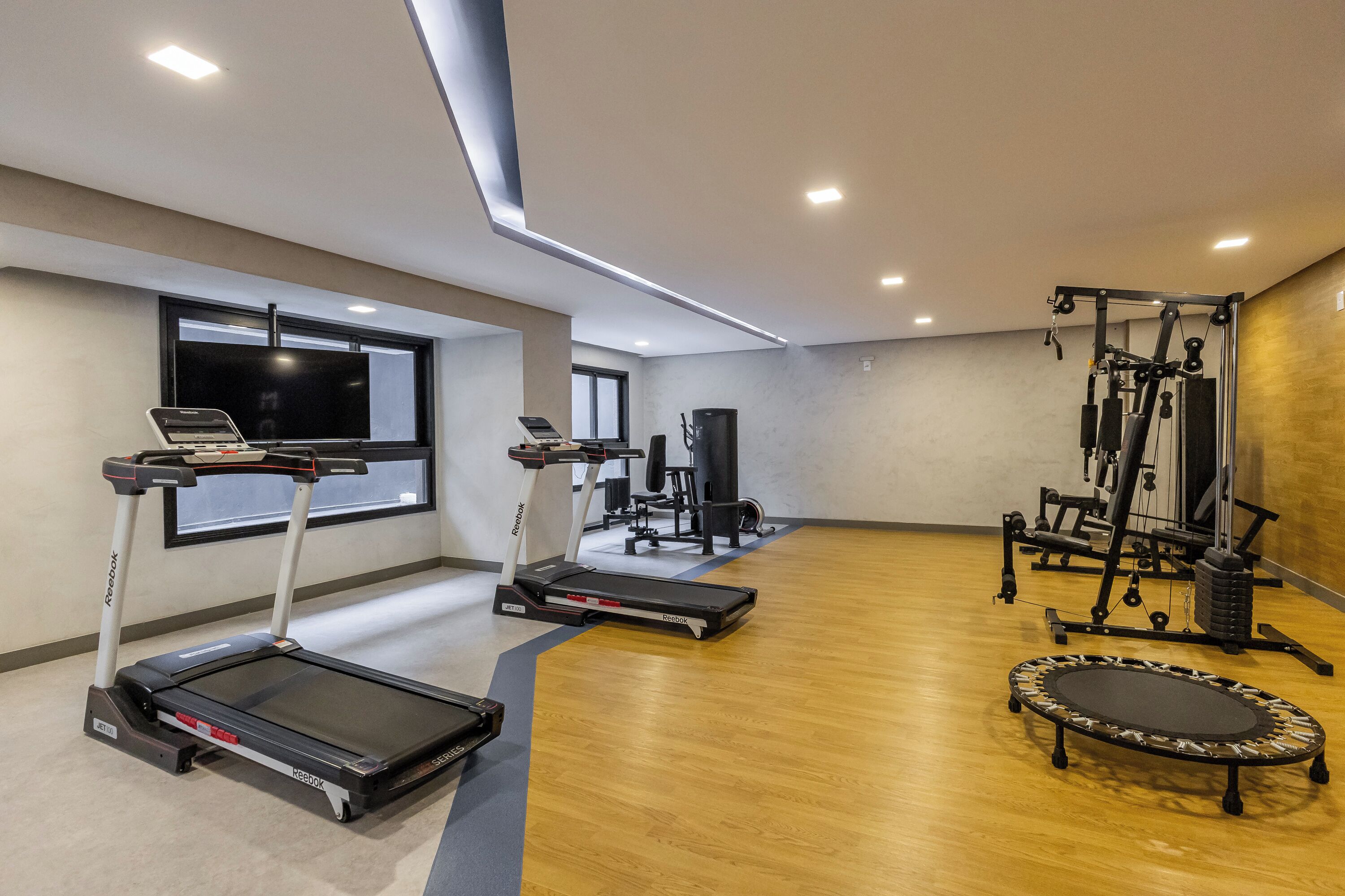 Une salle de sport équipée de tapis de course, d’un banc de musculation et d’un trampoline.