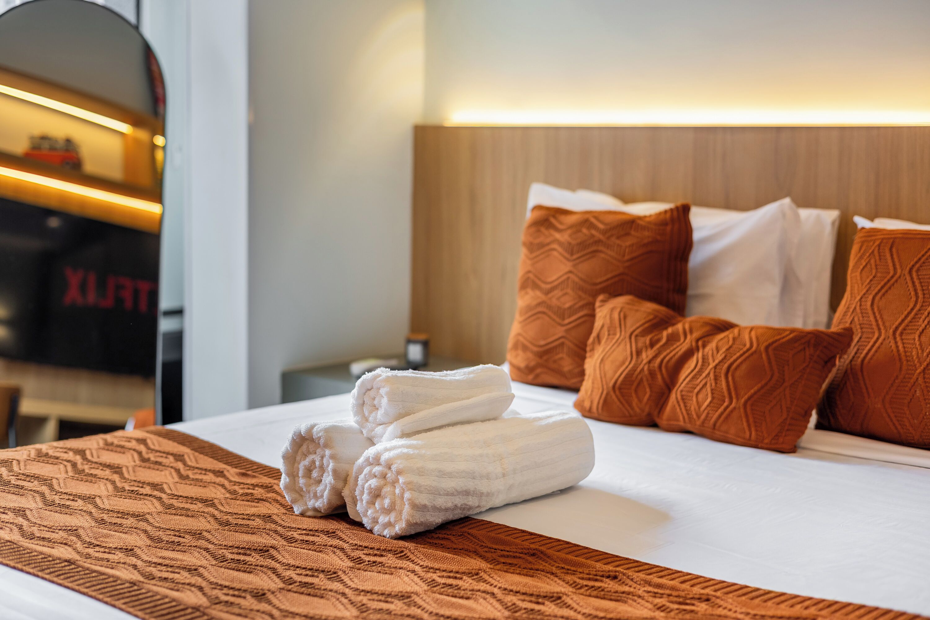 Un lit bien fait, avec du linge de lit blanc et marron, un plaid à motifs et plusieurs coussins.