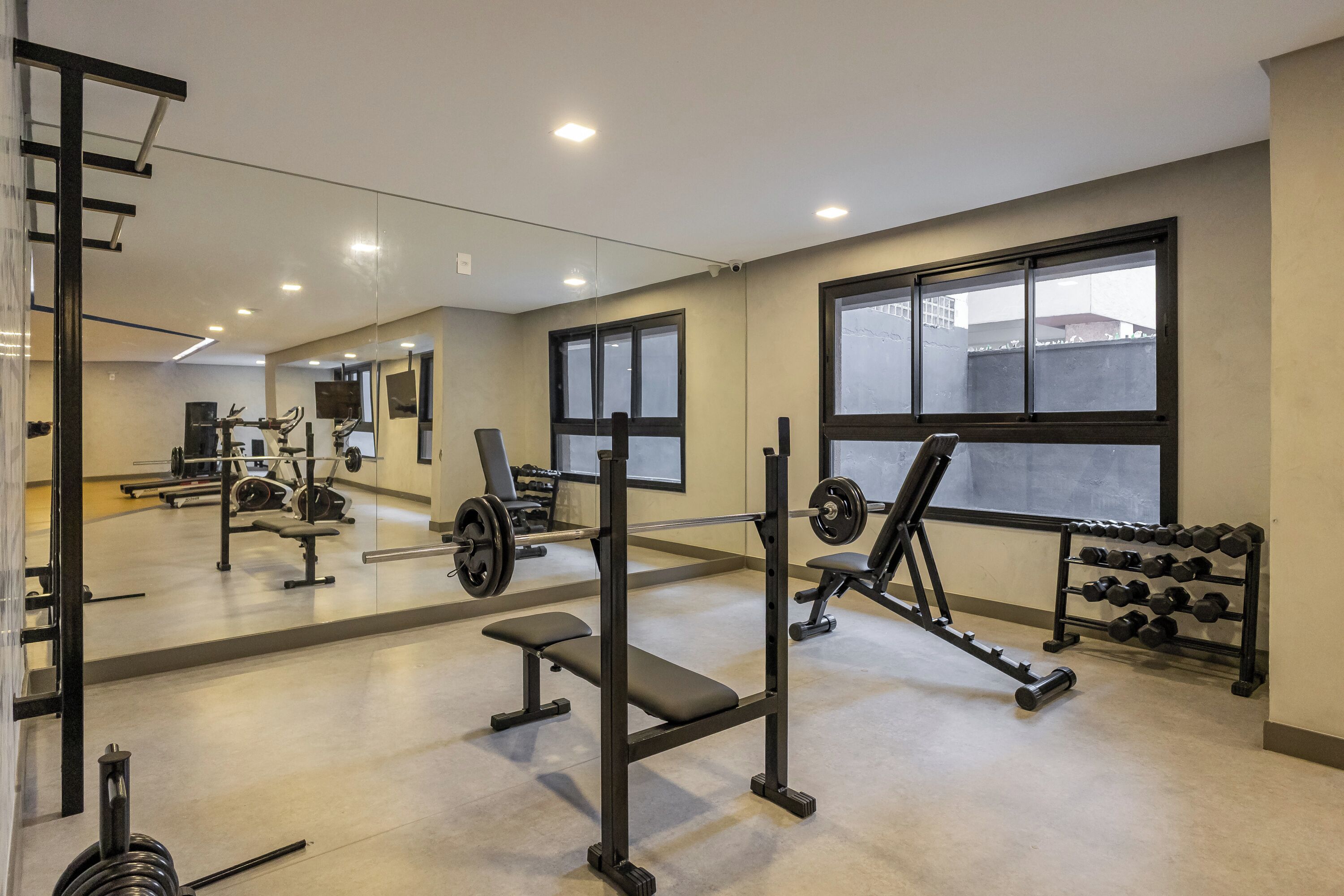 Ein Fitnessstudio mit unterschiedlichen Trainingsgeräten, großen Fenstern und einem Spiegel.