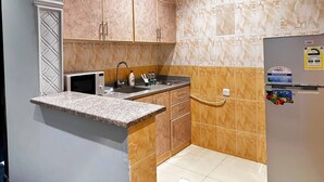 A compact kitchen with a granite countertop, a built-in microwave, and a refrigerator.