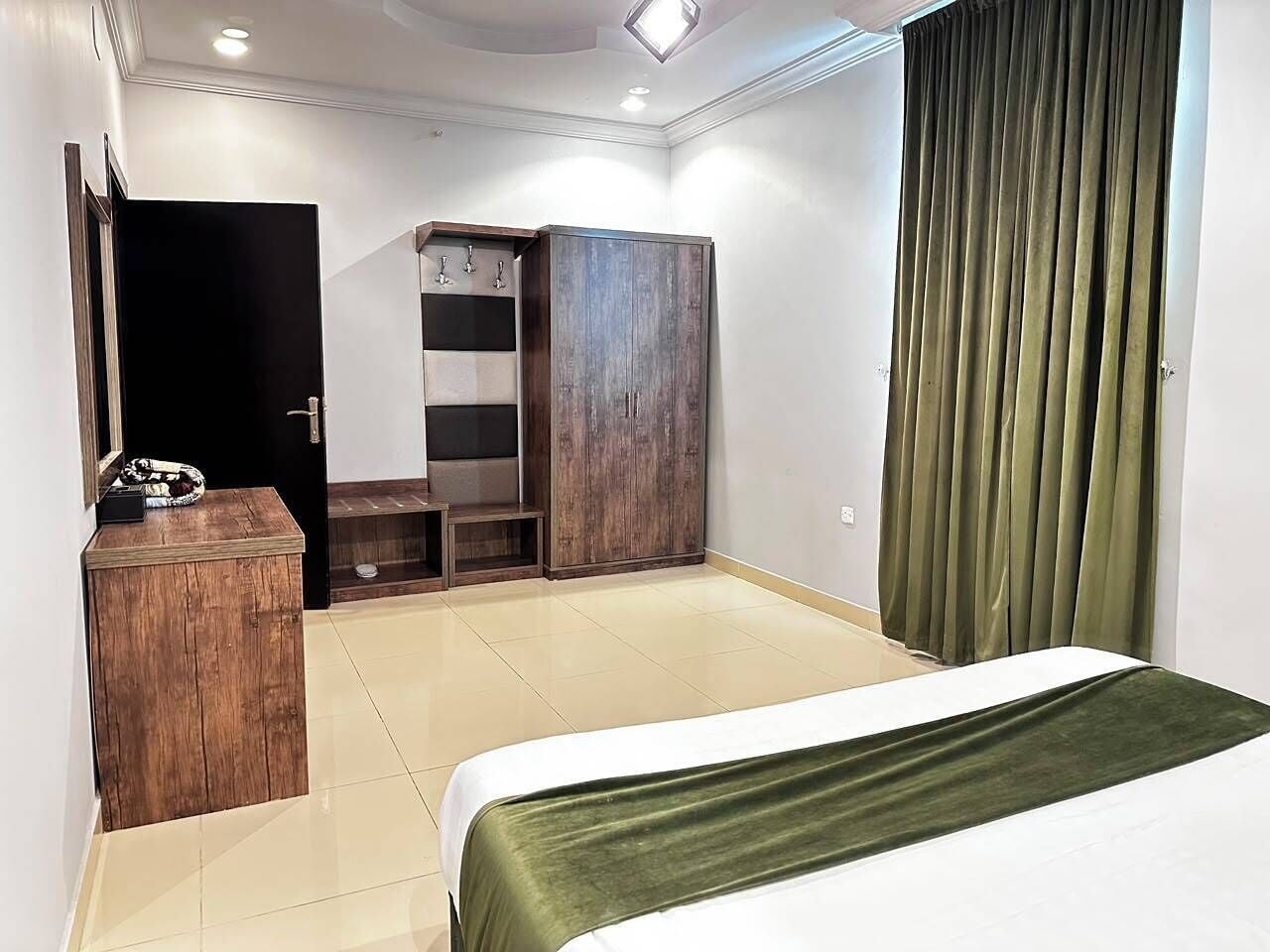 Una habitación de hotel con cama, armario, tocador con espejo y puerta.