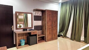 A room with a wooden desk, a mirror, a wardrobe, and a curtain.