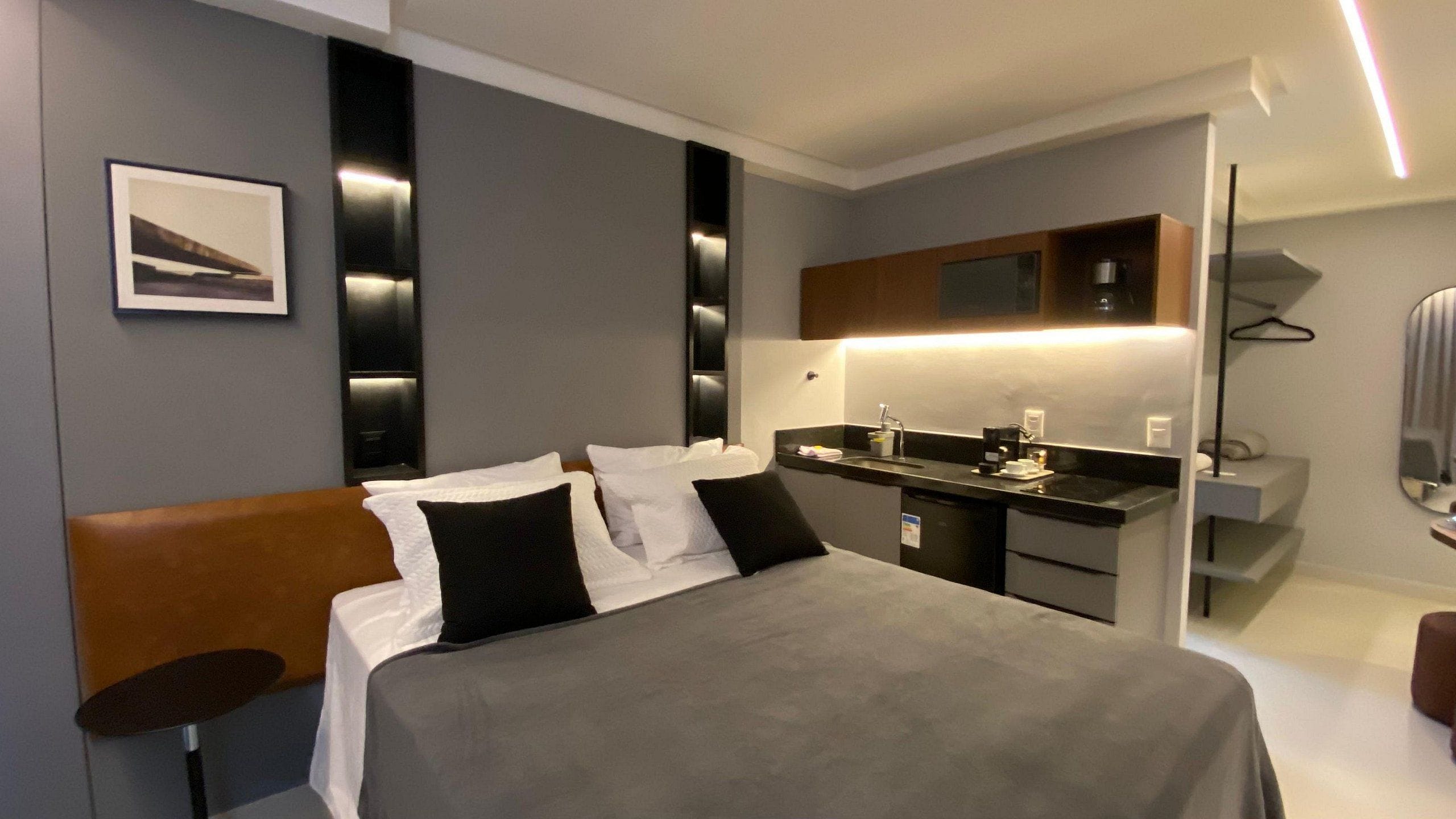 A modern hotel room with a bed, a small desk, and a mirror.