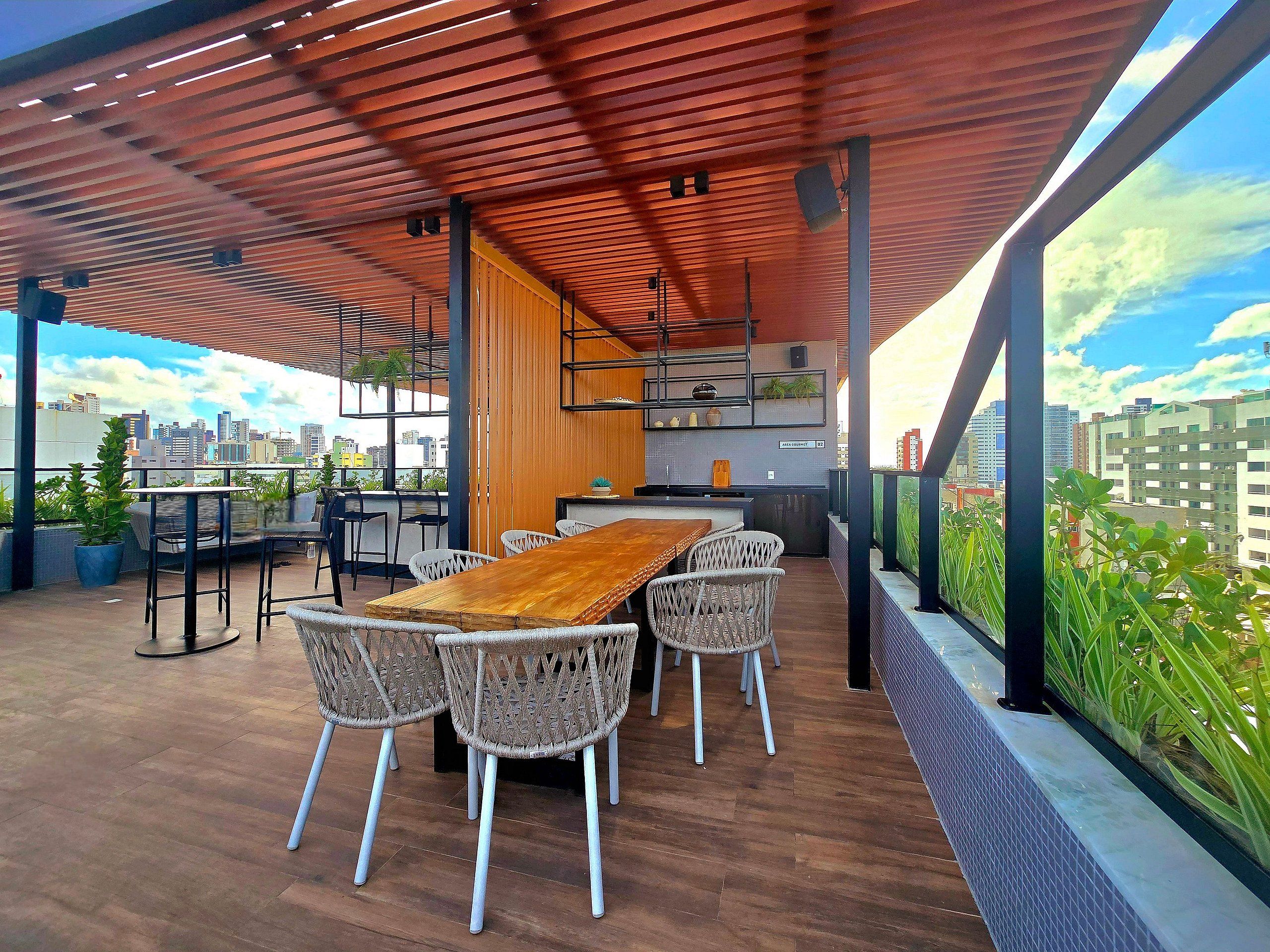 An outdoor dining area with a wooden table and wicker chairs, a kitchen area with a view of the city, and a covered space with a red ceiling.