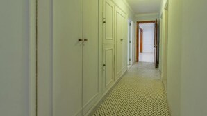 Un couloir étroit, avec un sol à motifs, des murs blancs et une porte au fond.