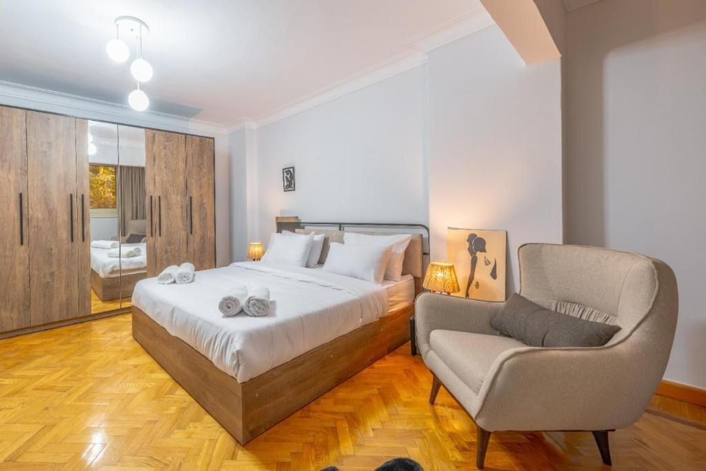 Un dormitorio con cama, mesita de noche, silla, armario y espejo.