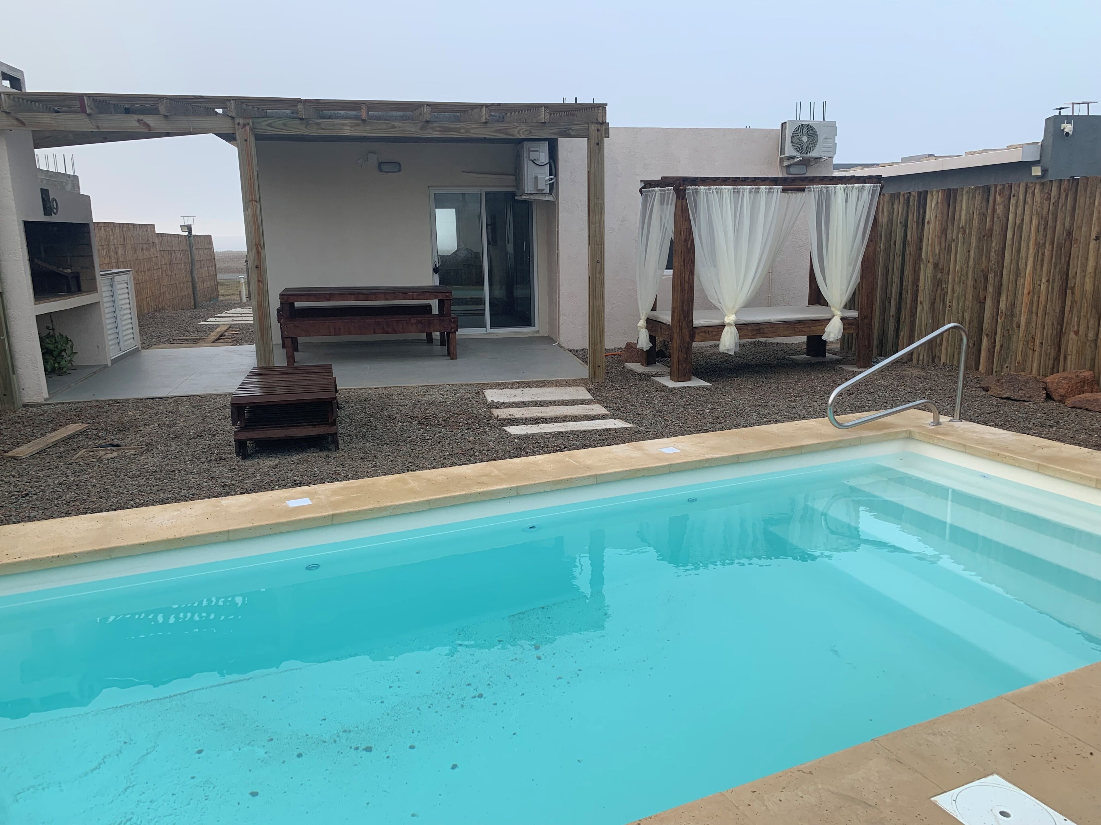 Una piscina con muelle de madera, una banca y un área de estar techada con vistas al cielo.