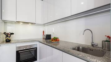 Una cucina moderna con mobili bianchi, un lavello in acciaio inossidabile e un forno integrato.