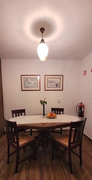 Un comedor con una mesa redonda, cuatro sillas, un florero con flores y dos cuadros en la pared.