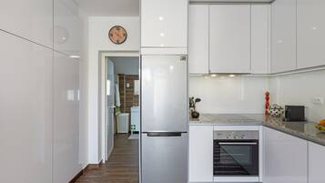 Une cuisine moderne avec des meubles blancs, un four encastré et un réfrigérateur en acier inoxydable.