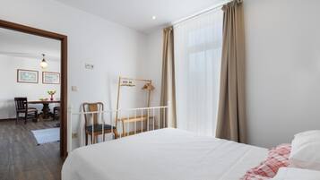 Een slaapkamer met een bed, een stoel, een bureau en een raam met gordijnen.