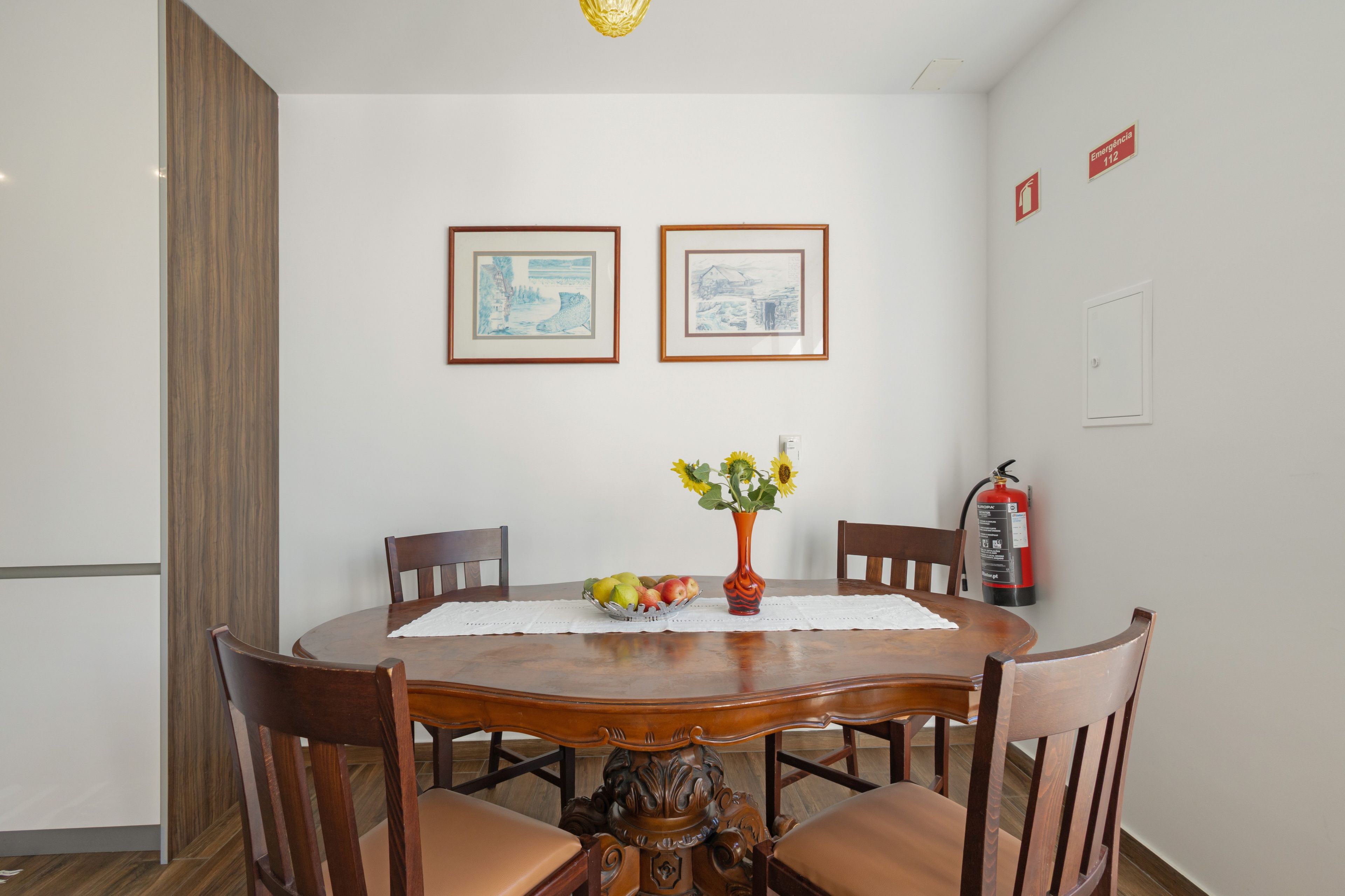 Un coin repas avec une table en bois, des chaises, un vase de fleurs et des tableaux encadrés accrochés au mur.
