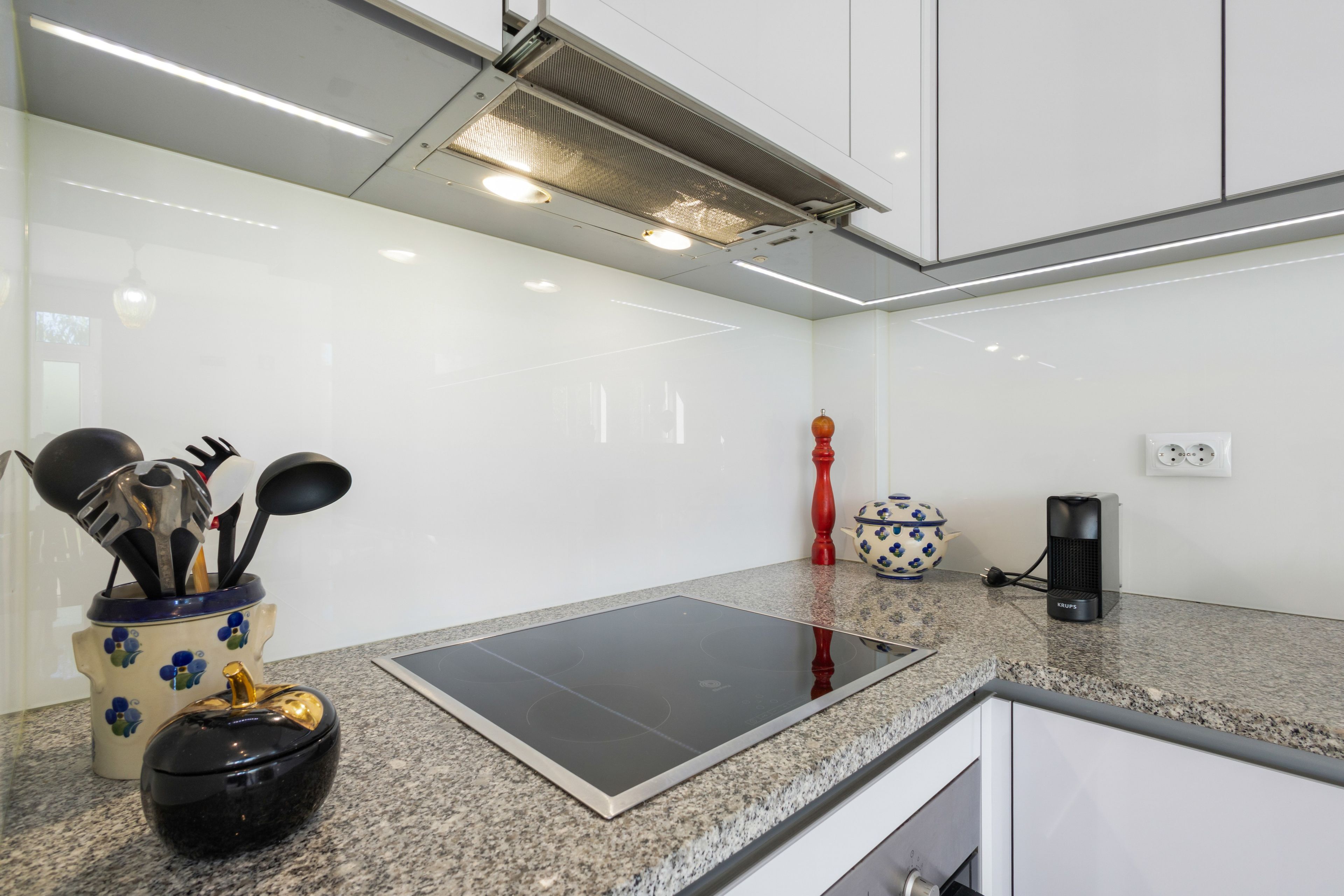 Uma cozinha moderna com bancada de granito, fogão por indução embutido, cafeteira e um vaso decorativo.