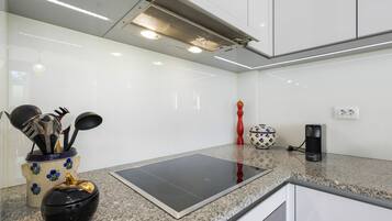 Uma cozinha moderna com bancada de granito, fogão por indução embutido, cafeteira e um vaso decorativo.