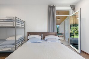 Une chambre moderne avec des lits superposés, un grand lit et une porte-fenêtre coulissante donnant sur un balcon.