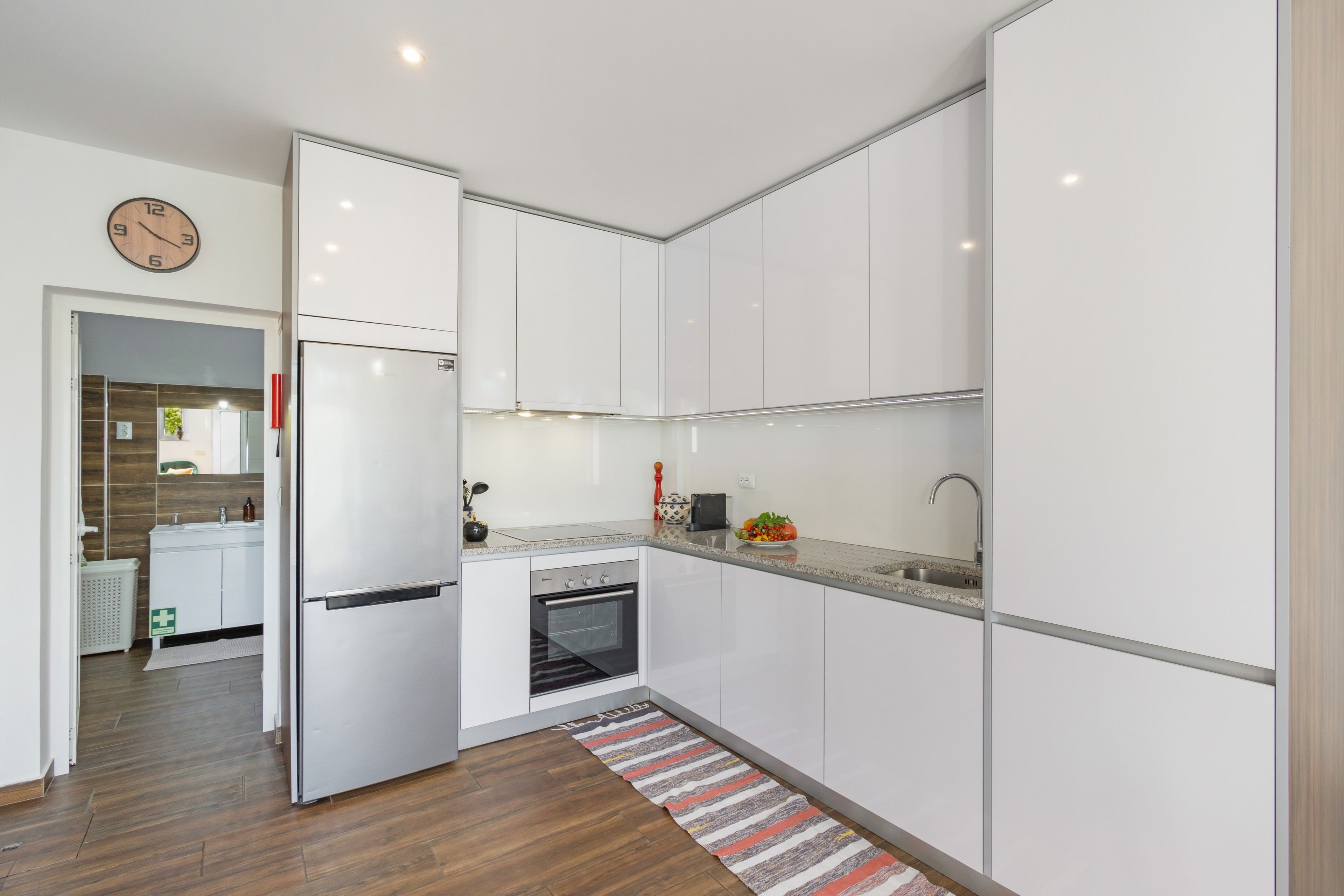 A modern kitchen with white cabinetry, a built-in oven, and a stainless steel refrigerator.