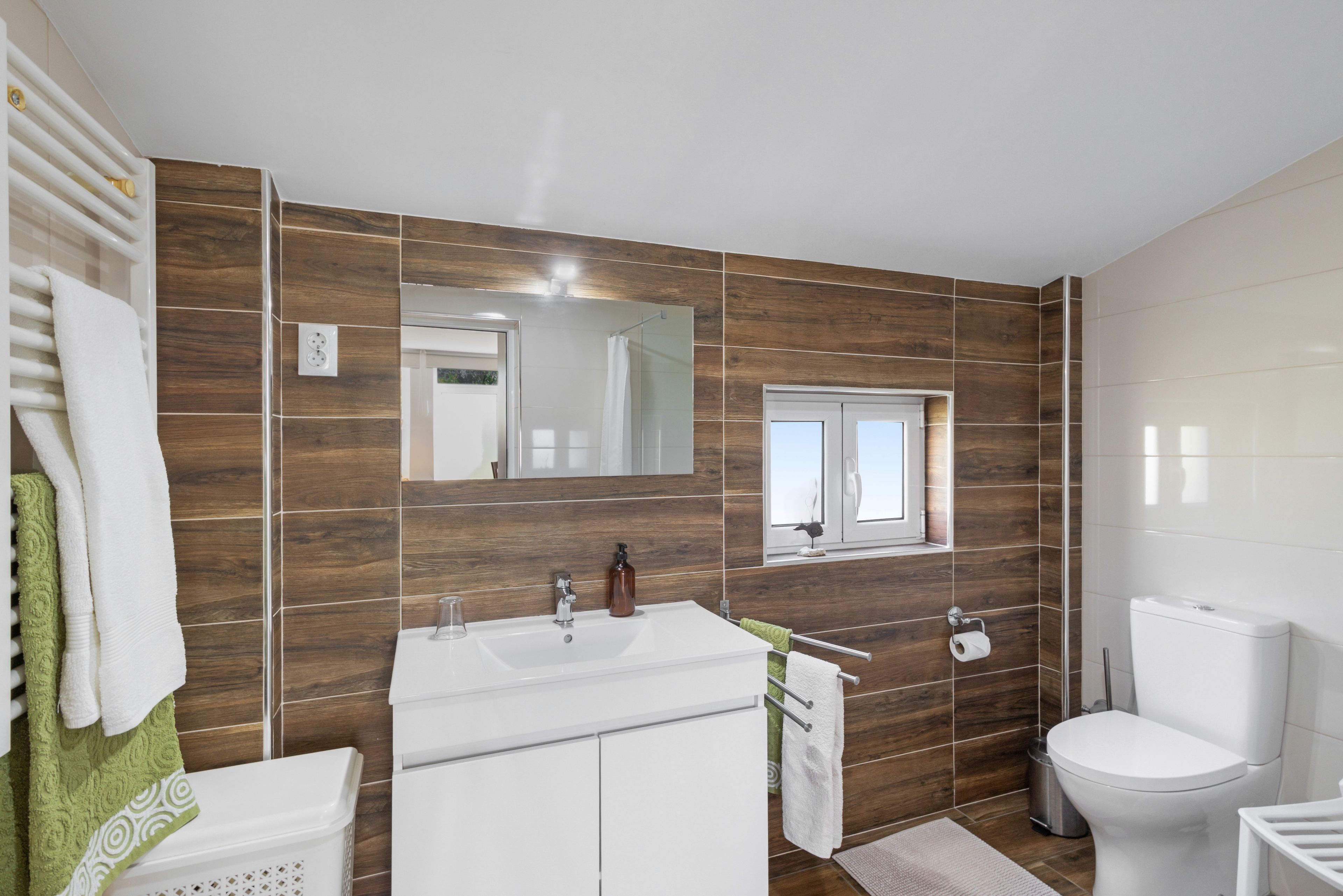 A modern bathroom with a large mirror, a white sink, and a toilet.