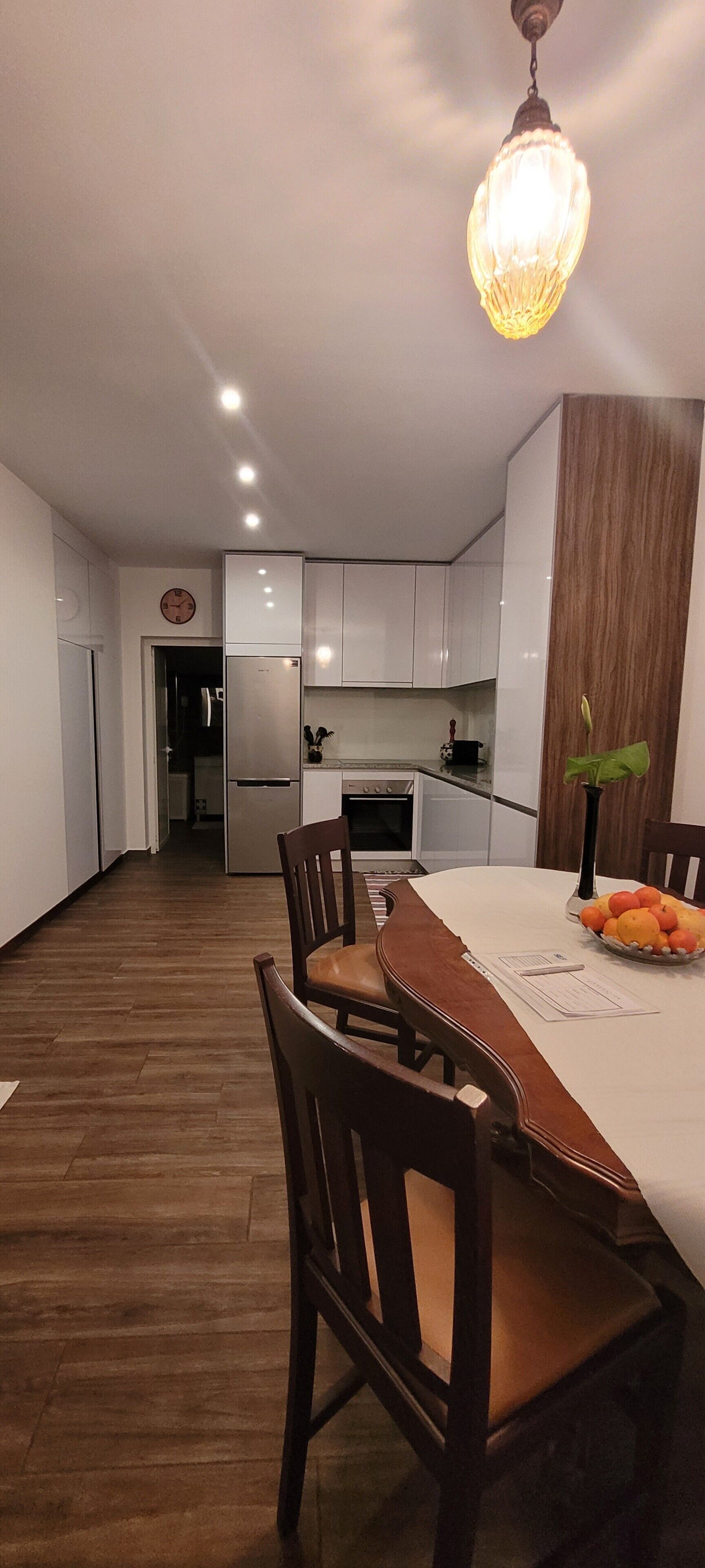 Une cuisine moderne avec des meubles blancs, une table à manger avec des chaises et un luminaire suspendu.