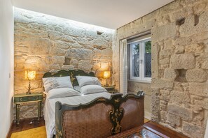 Une pièce avec un mur en pierre, un lit doté d’une tête de lit en bois, deux lampes de chevet et une fenêtre.