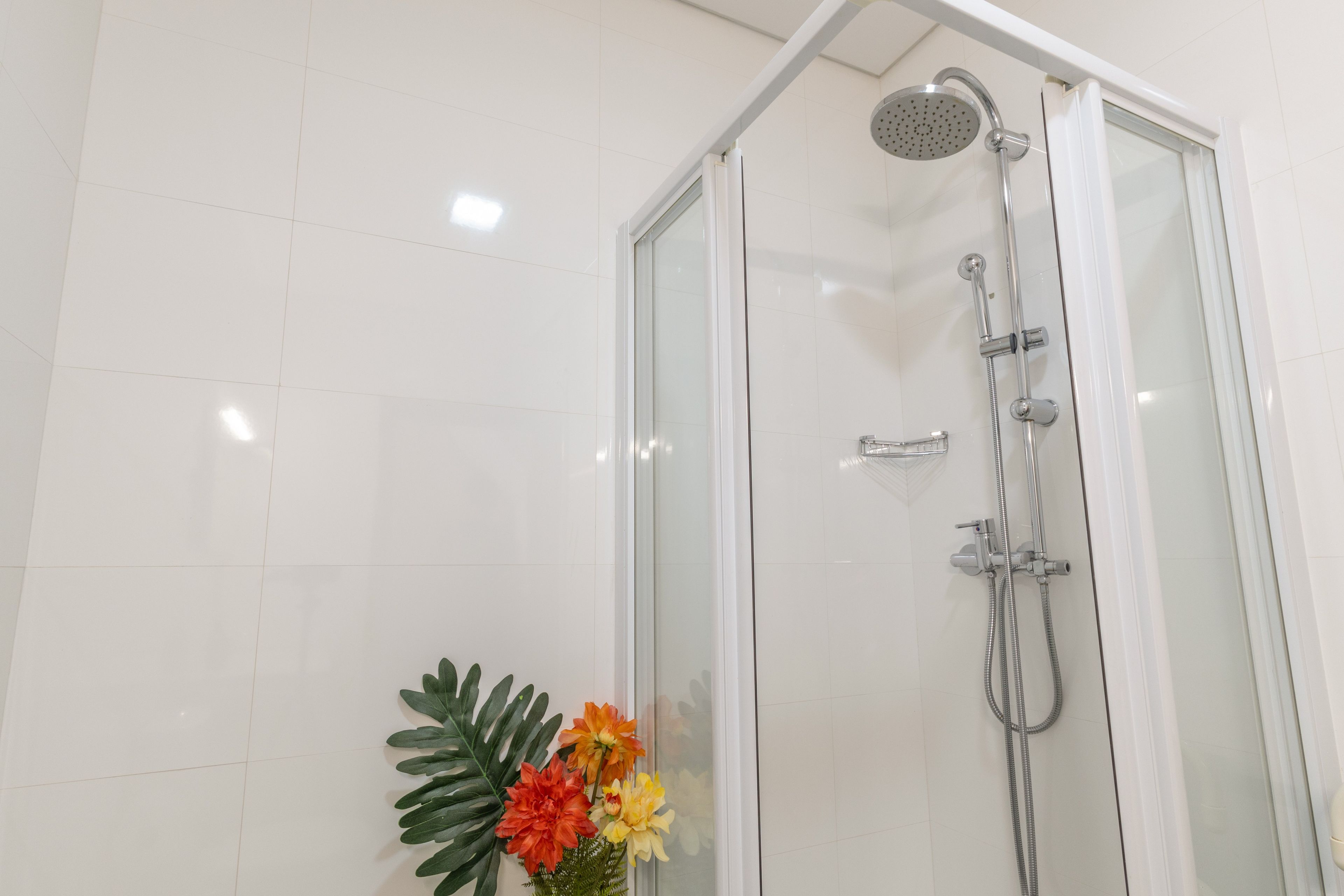 Une douche fermée par des parois en verre, dotée d’un pommeau de douche à main et d’un robinet mural.