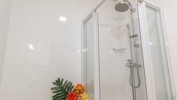 Une douche fermée par des parois en verre, dotée d’un pommeau de douche à main et d’un robinet mural.