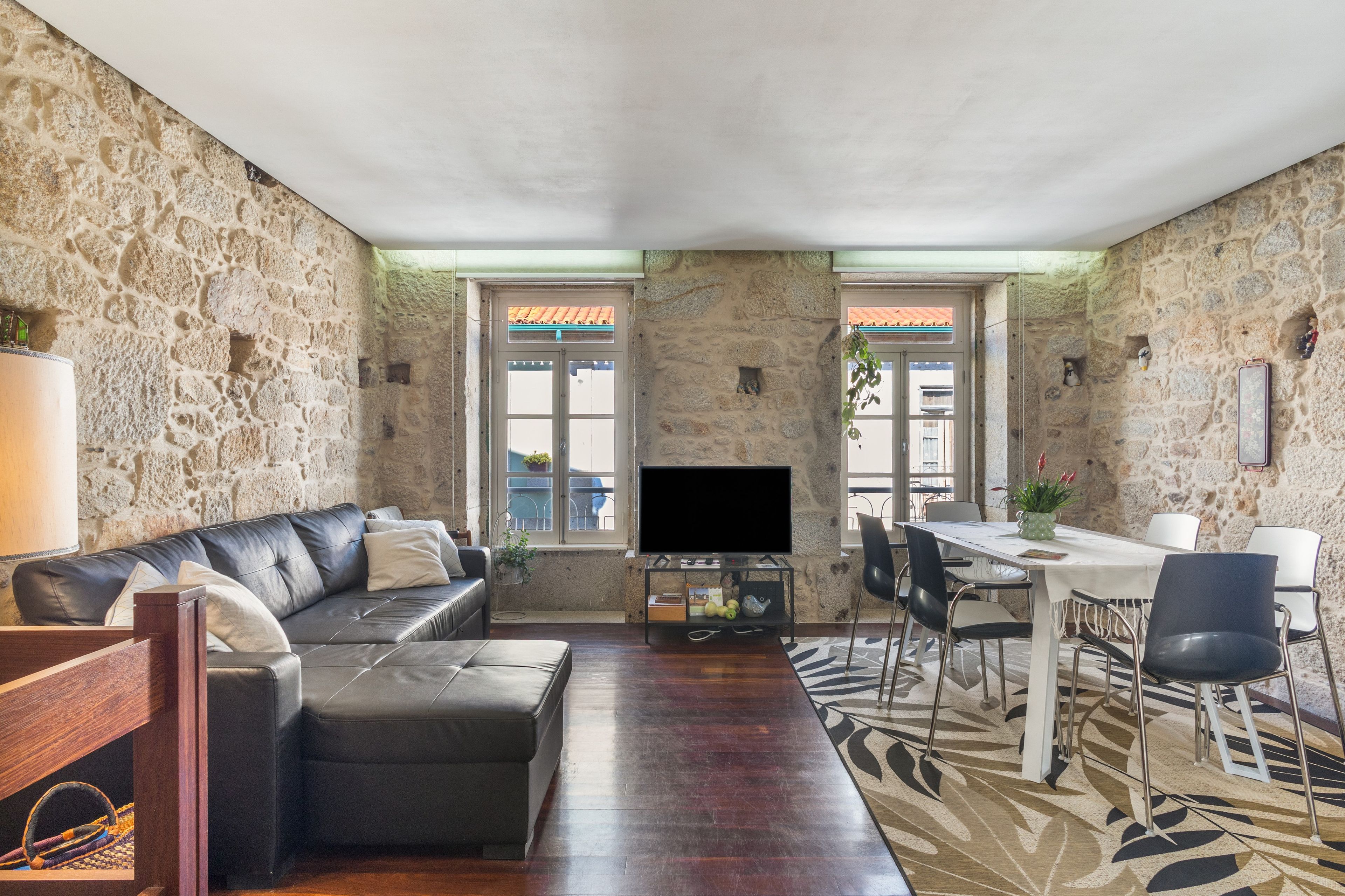 A living room with a stone wall, a leather sofa, a flat-screen TV, a dining table with chairs, and a patterned rug.