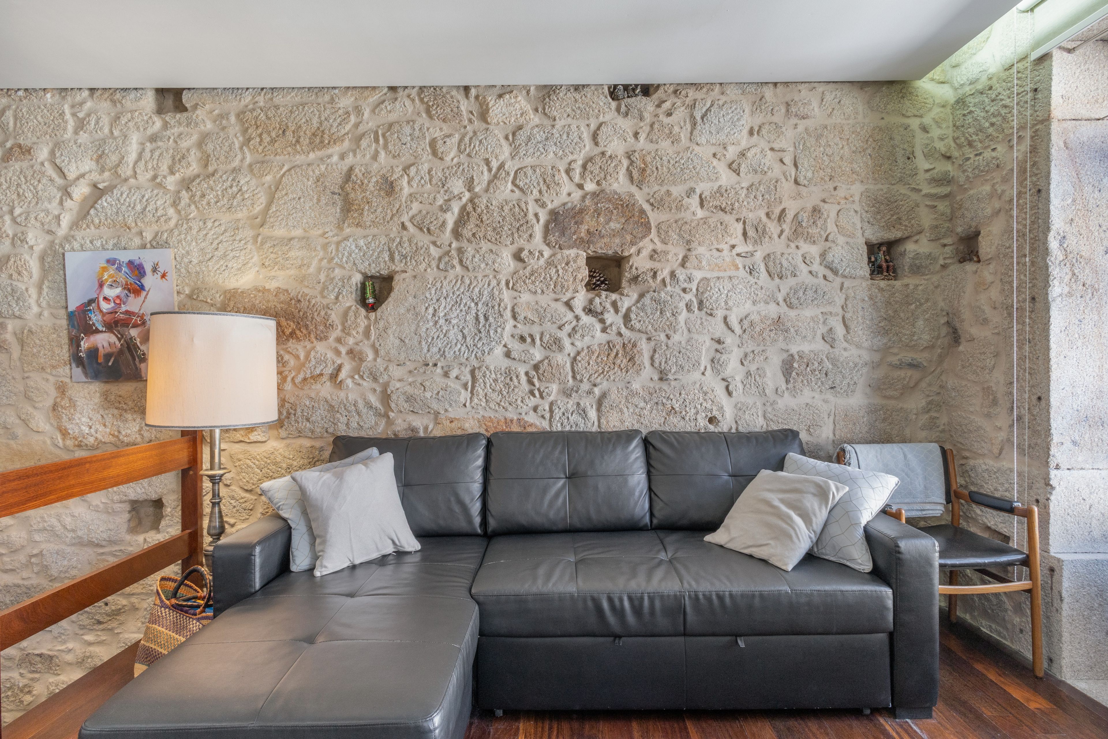 Una sala de estar moderna con una pared de piedra, un sofá de cuero, una silla de madera y una lámpara de pie.