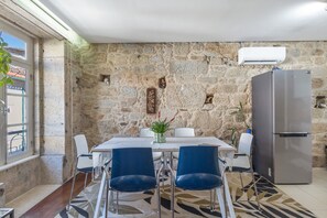 Un coin repas avec un mur en pierre, un réfrigérateur et une table avec des chaises.