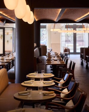 A restaurant with round tables, chairs, and hanging pendant lights.