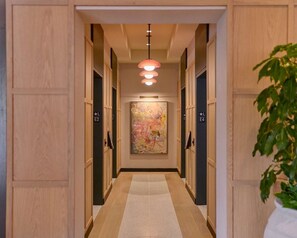 A hotel hallway with wooden paneling, a central light fixture, and a large abstract painting on the wall.