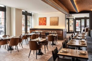A restaurant with a modern interior, featuring a mix of booths and tables, a herringbone floor pattern, and large windows allowing natural light.