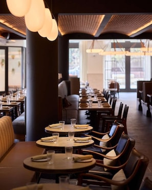 A restaurant with round tables, chairs, and hanging pendant lights.