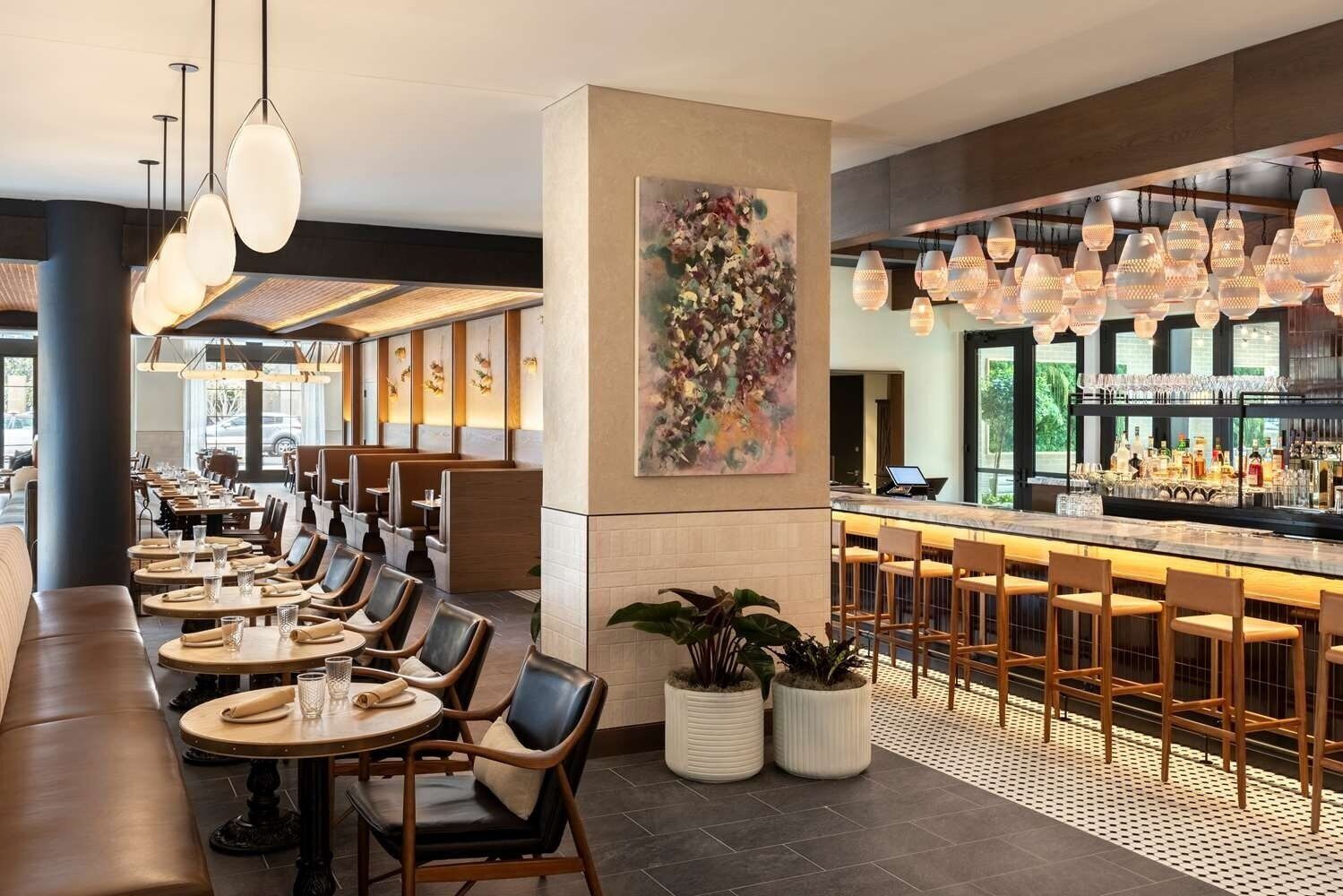 Ein modernes Restaurantambiente mit Barbereich, Sitzgelegenheiten und einem großen abstrakten Gemälde.