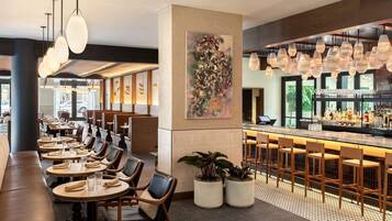 Ein modernes Restaurantambiente mit Barbereich, Sitzgelegenheiten und einem großen abstrakten Gemälde.
