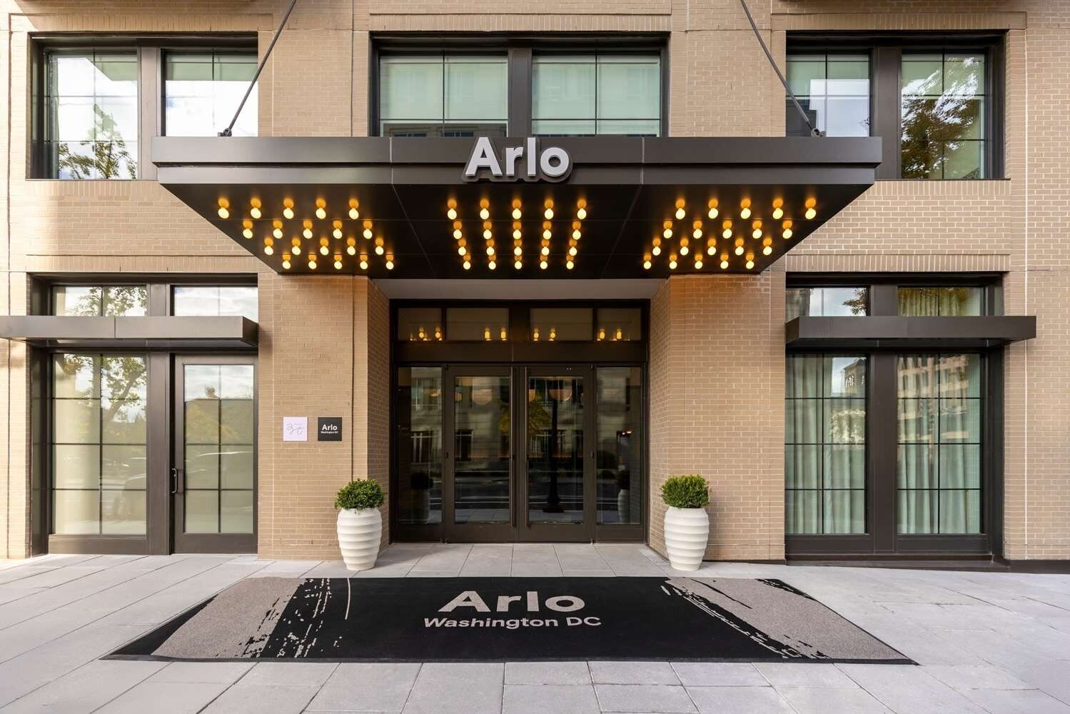 A hotel entrance with the name 'Arlo' above the doors, a black awning with lights, and a doormat with 'Arlo Washington DC' on it.