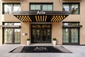 A hotel entrance with the name 'Arlo' above the doors, a black awning with lights, and a doormat with 'Arlo Washington DC' on it.