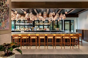 A bar area with multiple hanging light fixtures, a bar counter, and several bar stools.
