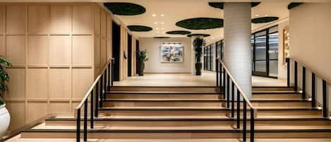 A staircase with wooden steps and black railings, leading to a landing with a potted plant and artwork.
