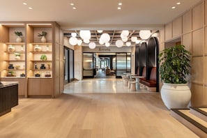 A modern hotel lobby with wooden paneling, a reception desk, seating area, and a large potted plant.
