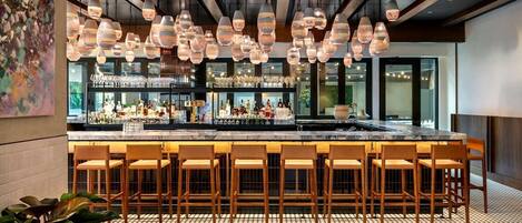 Un área de bar con múltiples lámparas colgantes, una barra y varios taburetes de bar.