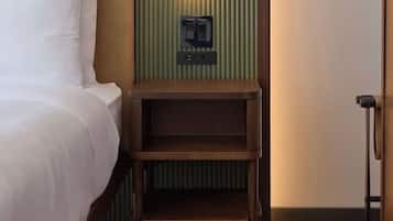 Ein Hotelzimmer mit einem Bett, einem Nachttisch aus Holz und einer an der Wand montierten Steckdose.