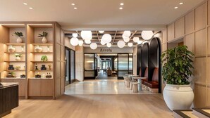 Un hall d’hôtel moderne avec des panneaux de bois, un comptoir d’accueil, un espace salon et une grande plante en pot.