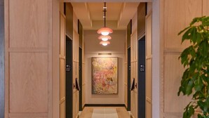 Un couloir d’hôtel avec des lambris en bois, un luminaire central et un grand tableau abstrait accroché au mur.