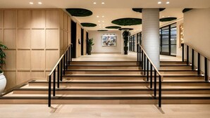 Un escalier avec des marches en bois et des rampes noires, menant à un palier agrémenté d’une plante en pot et d’une œuvre d’art.