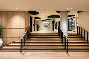 A staircase with wooden steps and black railings, leading to a landing with a potted plant and artwork.