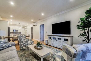 Ein Wohnzimmer mit einem Flachbildfernseher, gemusterten Sofas, einem Couchtisch und einem Essbereich im Hintergrund.