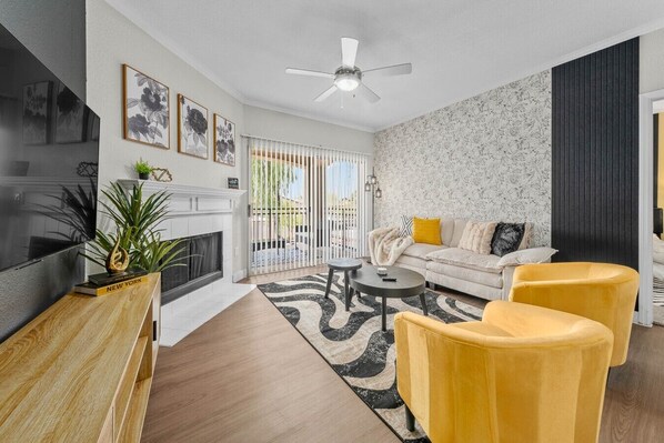 Un salon moderne avec une cheminée, un canapé, des fauteuils jaunes et un téléviseur.